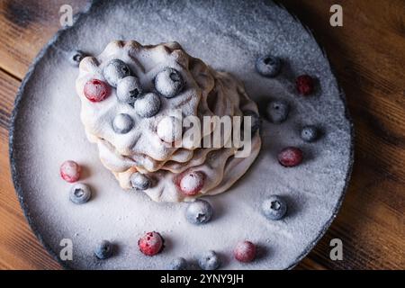 Waffle belgi con mirtilli rossi e mirtilli cosparsi di zucchero a velo su un tavolo di legno su un piatto nero. Foto di alta qualità Foto Stock