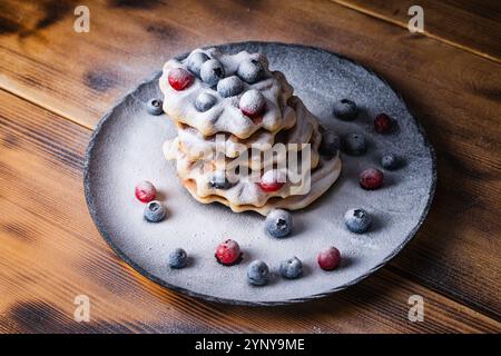 Waffle belgi con mirtilli rossi e mirtilli cosparsi di zucchero a velo su un tavolo di legno su un piatto nero. Foto di alta qualità Foto Stock