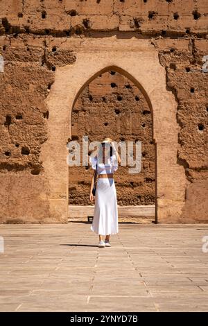 Giovane donna dai capelli scuri con abito bianco e cappello in posa nel cortile esterno del Palazzo El Badii di Marrakech, Marocco Foto Stock