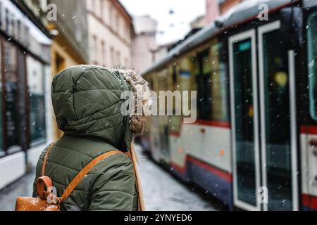 Pendolari che viaggiano con i mezzi pubblici in città durante la stagione invernale. Donna in giacca a cappuccio che sale su un tram alla fermata dell'autobus sulla strada Foto Stock