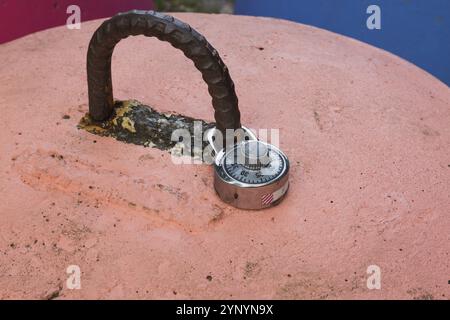 Primo piano del lucchetto a combinazione cromato bloccato fissato al manico in acciaio arrugginito su un blocco a campana in cemento verniciato color salmone, Quebec, Canada, NOR Foto Stock