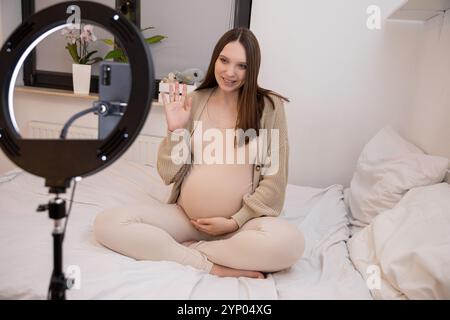 Una donna incinta radiosa sorridente gioiosamente al camera da letto in un ambiente accogliente pieno di calore Foto Stock