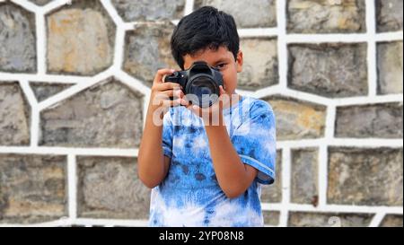 Un ragazzo latino di 10 anni dalla pelle scura impara a usare una macchina fotografica professionale, sogna e immagina di lavorare da adulto Foto Stock