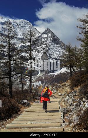 Perduto nella bellezza delle maestose vette di Yading, un giovane avventuriero si dirige verso le montagne, abbracciando il viaggio tanto quanto la destinazione. Foto Stock