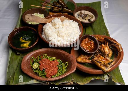 Un menu fisso per pranzo con riso al vapore, pollo fritto, zuppa di verdure e sambal (salsa al peperoncino), servito su piatti di argilla con foglie di banana fresche. Foto Stock