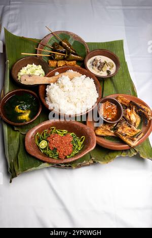 Un menu fisso per pranzo con riso al vapore, pollo fritto, zuppa di verdure e sambal (salsa al peperoncino), servito su piatti di argilla con foglie di banana fresche. Foto Stock