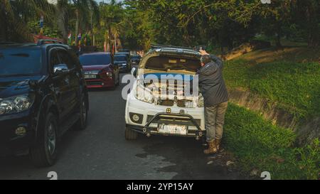 Balikpapan, Indonesia - 3 settembre 2024. Un uomo esamina il vano motore della sua auto, che è parcheggiato sul lato della strada. Foto Stock