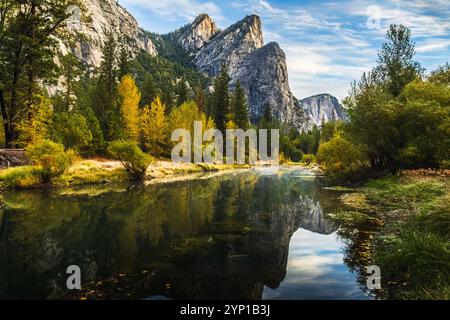 Vista del fiume Merced nel Parco Nazionale di Yosemite, California, con le vette dei Three Brothers in autunno; le vette e il fogliame autunnale si riflettono in acque calme Foto Stock