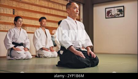 Inginocchiarsi, salutare e persone in studio di arti marziali per esercitarsi, allenarsi o fare lezioni di autodifesa. Cultura, karate e gruppo di studenti con rispetto Foto Stock