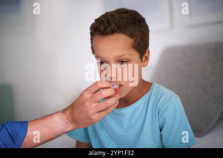 Padre, mani e medicina per il bambino malato in casa, aiutando il figlio e farmaci liquidi per il trattamento dell'influenza. Papà, ragazzo e supporto con gli antibiotici Foto Stock