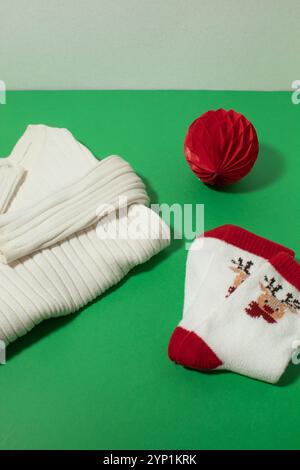 Maglione invernale bianco con calze natalizie e ornamenti rossi su sfondo verde Foto Stock