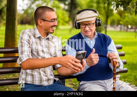 Ritratto di nonno felice e nipote nel parco. Stanno trascorrendo del tempo insieme e si divertono. Il vecchio sta ascoltando della musica. Foto Stock