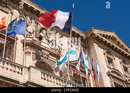 Marsiglia. Francia - 27 novembre 2024: Municipio di Marsiglia con bandiere francesi che sventolano in alto, sottolineando i dettagli in pietra e il significato storico Foto Stock