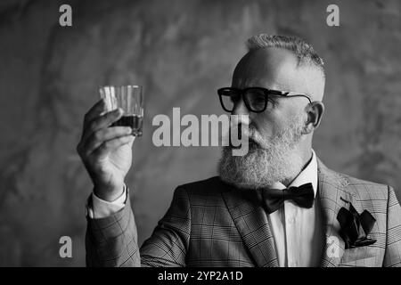 Foto ravvicinata di un serio pensivo fiducioso soddisfatto barbuto ricco imprenditore produttore di vino che guarda il bicchiere con whisky Foto Stock