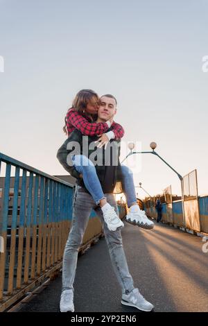 Incantevole abbraccio pomeridiano: Una giovane coppia catturata in un gioioso affetto su un ponte. Foto Stock