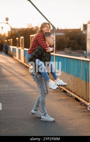 Giovane coppia che si gode un momento di gioco su un ponte durante il tramonto. Foto Stock