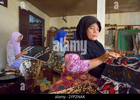 Donne che usano uno strumento simile a una penna (cantando), per applicare cera calda liquida nel processo di fabbricazione del batik, laboratorio di batik di Wirakuto, Pekalongan, isola di Giava, indonesi Foto Stock