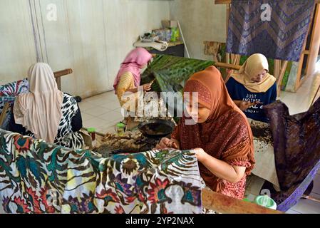 Donne che utilizzano uno strumento simile a una penna (cantando) per applicare cera calda liquida nel processo di fabbricazione del batik, laboratorio di batik di Wirakuto, Pekalongan, isola di Giava, Indonesia Foto Stock