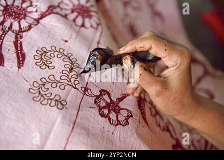 Donna che utilizza uno strumento simile a una penna (cantando) per applicare cera calda liquida per creare un motivo sul tessuto prima della tintura, laboratorio di Kidang Mas Batik House, Lasem Foto Stock