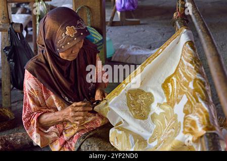 Donna che usa uno strumento simile a una penna (cantando) per applicare cera calda liquida per creare un motivo su tessuto senza disegno preliminare, Nyah Kiok batik House, Lasem, J. Foto Stock