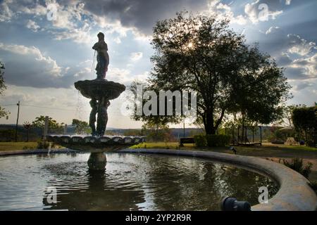 Una fontana con una statua di una donna e due bambini. L'acqua è ferma e il cielo è nuvoloso Foto Stock