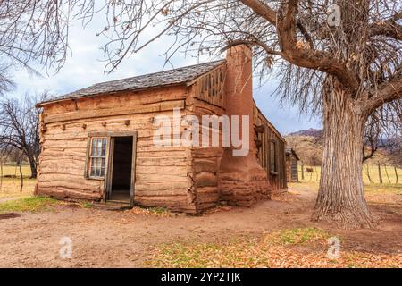 Una piccola, vecchia casa con un camino si trova in un campo. La casa è fatta di legno e ha un aspetto rustico. L'area circostante è per lo più vuota, con o Foto Stock