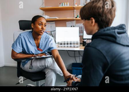 Donna medico professionale consolando il paziente adolescente mentre seduto in sala esame presso la clinica Foto Stock