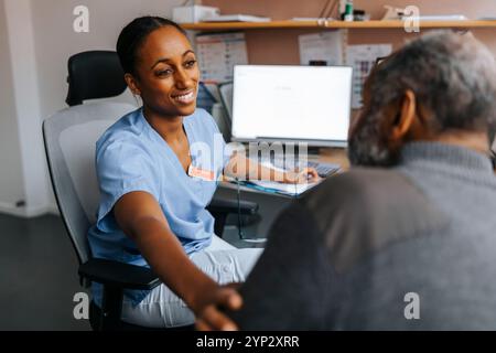 Medico sorridente che consola paziente anziano seduto sulla sedia nella sala esame medico Foto Stock