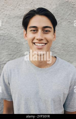 Ritratto di un giovane sorridente con t-shirt grigia vicino al muro Foto Stock