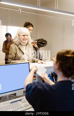 Donna anziana sorridente prenotazione appuntamento medico alla reception in ospedale Foto Stock