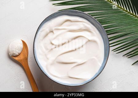 Yogurt bianco fresco al cocco. Ciotola di yougurt greco e foglie di palma su sfondo bianco, vista dall'alto. Foto Stock