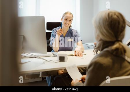 Medico donna seduta con paziente anziano alla scrivania in clinica Foto Stock