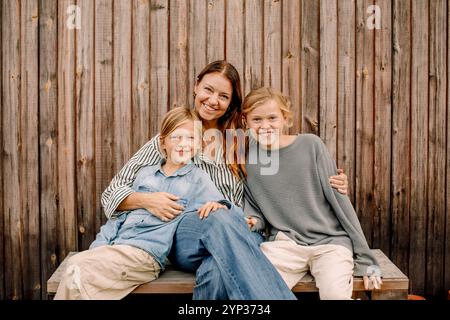 Ritratto di donna sorridente seduta con figli sulla panchina davanti a una recinzione di legno Foto Stock
