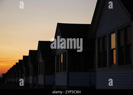 Una fila di cottage in affitto è in silhouette, ad eccezione delle finestre che riflettono il tramonto, lungo la riva di Cape Cod Foto Stock