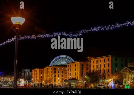 Una splendida vista notturna dell'Albert Dock di Liverpool adornata da luci festose. Il caldo bagliore degli edifici portuali contrasta splendidamente con la scintilla Foto Stock