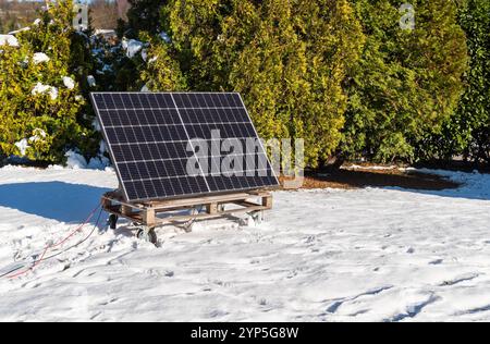 Pannello fotovoltaico su un pallet di legno nel giardino innevato della casa durante l'inverno. Concetto di energia verde. Foto Stock