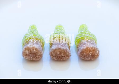 Foto dettagliata di tre piccole bottiglie di cola di gomma zuccherata in una vista frontale su un piatto bianco pulito. Concetto di dolce colorato e luminoso Foto Stock