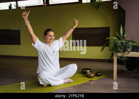 Donna positiva che fa ego o mudra di personalità, stile di vita sano e pratica Kundalini yoga seduto in posizione di loto con gli occhi chiusi sul tappetino in me Foto Stock