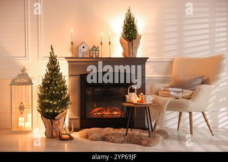 Piccoli alberi di abete rosso decorati con luci natalizie vicino al caminetto interno Foto Stock