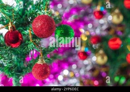 Una vista ravvicinata di un albero di Natale splendidamente decorato adornato con vivaci ornamenti rossi e verdi scintillanti, adagiato su un colorato sfondo bokeh Foto Stock