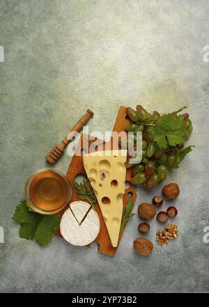 Formaggio con grandi buchi, emmental, maasdam, formaggio brie, su un tagliere, con uva e miele, noci, antipasto al vino, vista dall'alto Foto Stock