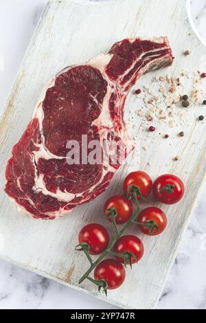 Costolette crude, bistecca di cowboy, su un tagliere di legno bianco, tavolo in marmo, vista dall'alto, niente persone Foto Stock