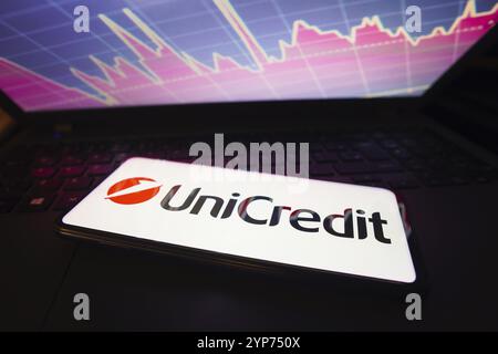 In questa immagine viene mostrato l'UniCredit visualizzato su uno schermo di uno smartphone, con una rappresentazione grafica del mercato azionario sullo sfondo Foto Stock