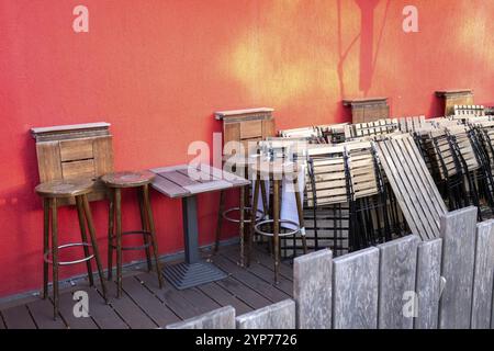 Area esterna con sgabelli in legno e un tavolo contro una vivace parete rossa Foto Stock