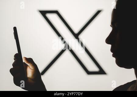 In questa foto, la silhouette di una donna tiene uno smartphone con il nuovo logo Twitter (X) sullo sfondo Foto Stock