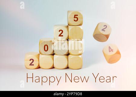 Felice anno nuovo 2025, il numero è scritto su cubi di legno impilati, i vecchi numeri stanno cadendo, sfondo chiaro, spazio di copia Foto Stock