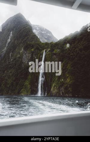 Vista dalla barca di un'alta cascata circondata da montagne e nebbia, Milford Sound, nuova Zelanda, Oceania Foto Stock