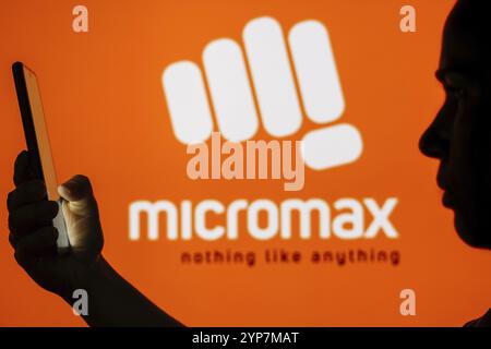 In questa illustrazione fotografica, il logo Micromax Informatics è visibile sullo sfondo di una donna sagomata che tiene in mano un telefono cellulare Foto Stock