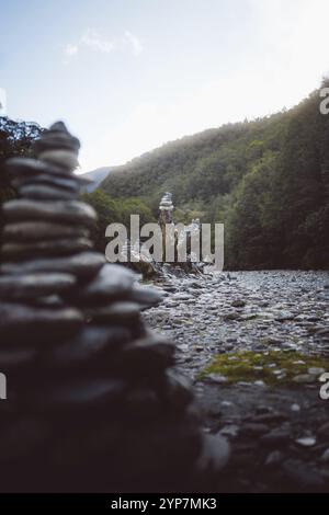 Primo piano di cairns sulla riva del fiume, circondato da alberi e montagne, West Coast, nuova Zelanda, Oceania Foto Stock