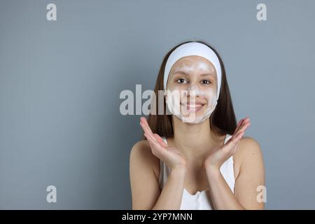 Adolescente con schiuma detergente sul viso su sfondo grigio, spazio per il testo. Trattamento dell'acne Foto Stock